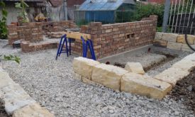 Während die Mauerarbeiten fortschreiten, entsteht nebenher eine Natursteinmauer aus Sandstein.